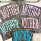 Gray marbled coasters with 'MOTHER' text in various colors on a white surface.