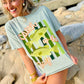 Woman wearing a light blue t-shirt with fish graphics and text on a rocky beach.