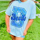 Person wearing a light blue t-shirt with 'Devils' printed on it, standing on a grassy field.