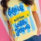 Person wearing a yellow t-shirt with blue text on a pink and white striped background