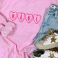 A pink embroidered sweatshirt with the word 'BABE' in heart shape on the front, displayed flat with a pair of blue jeans and white sneakers on top.