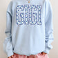 Light blue sweatshirt with 'GIGI' printed on it, worn by a person with red checkered shorts.