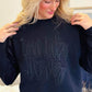 Woman wearing a black sweatshirt with Black monocromatic Love like Jesus , sitting on a couch.