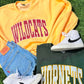 Yellow sweatshirt with 'WILDCATS' text, green shirt with 'HORNETS' text, white sneakers, and blue shorts on grass.