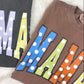 Two sweatshirts with colorful 'MAMA' text on a white surface