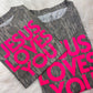 Two folded shirts with 'Jesus Loves You' Puff neon vinyl text on a fluffy white surface