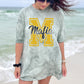 Woman wearing a gray dress with a yellow 'M' and the word 'Mafia' on a beach.