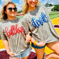 Two women wearing 'Bulldogs' and 'Devils' metallic puff shirts on a sports field.