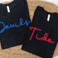 Two black leopard patterned t-shirts with 'Devils' in blue and 'Tide' in red on a woven surface.