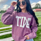 Woman wearing a purple 'TIDE' sweatshirt on a sports field