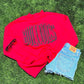 Red shirt with 'Bulldogs' text, sunglasses, and denim shorts on grass