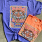 A graphic tee with a melon and violet color scheme featuring The Heavens Are Roaring Psalm 19:1 and a tiger design, laid flat on a surface.