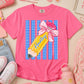 Pink t-shirt with a pencil graphic and 'Haley' text, surrounded by stationery items on a light background.